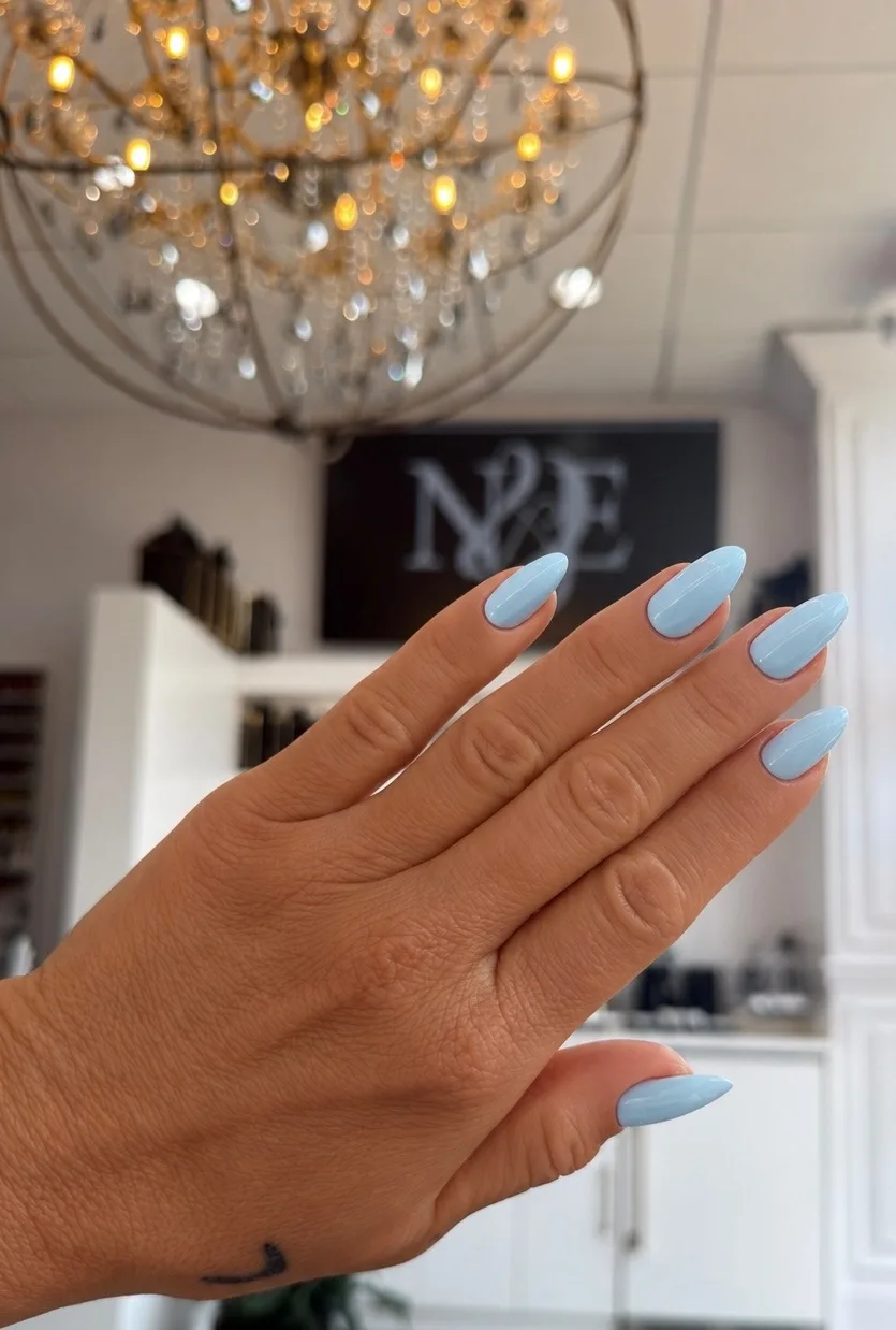Sky-blue almond nails beneath the crystal chandelier and the N&E sign at Ridgewood Nail Club.
