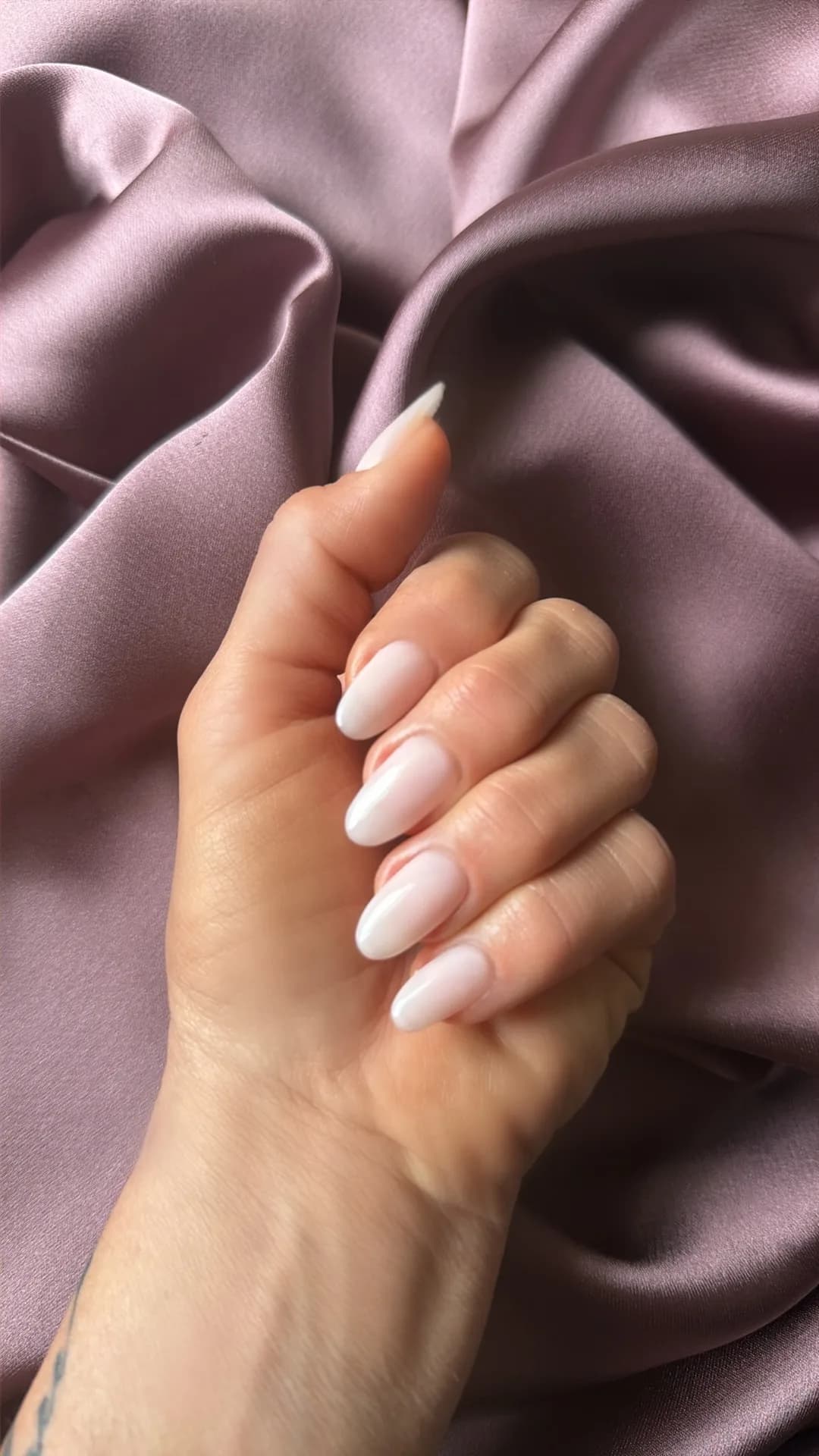 Soft milky-white almond manicure resting on dusty-mauve silk.